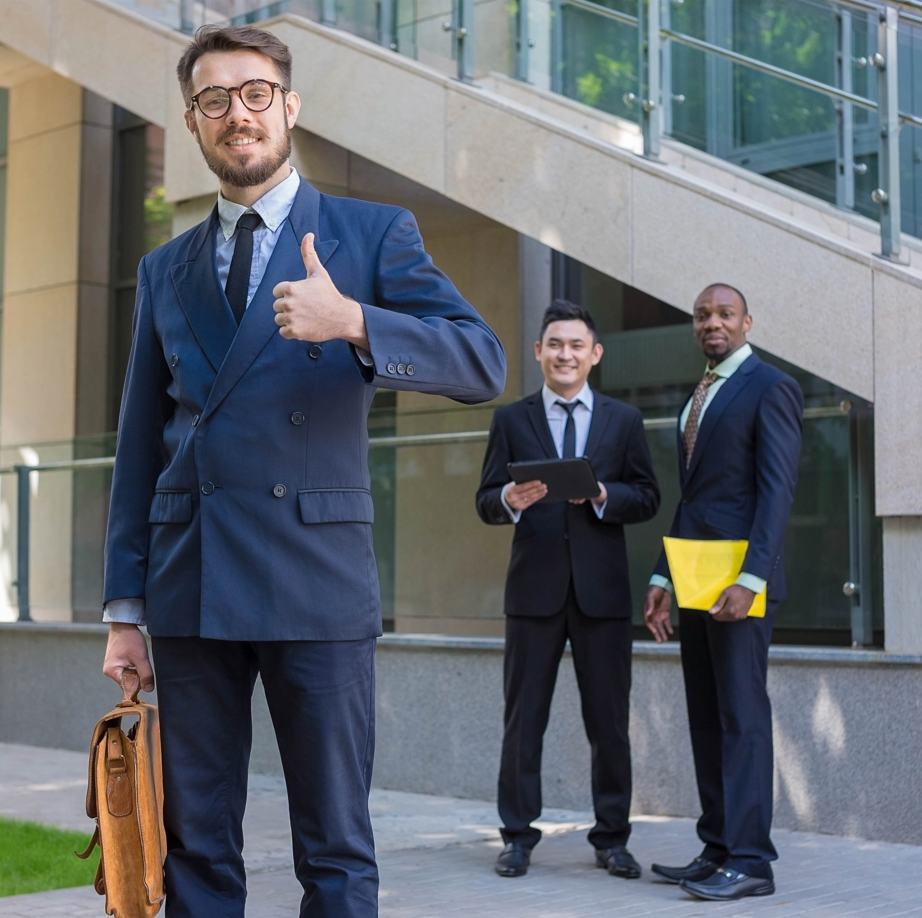 Confident businessman giving a thumbs-up with two colleagues in the background